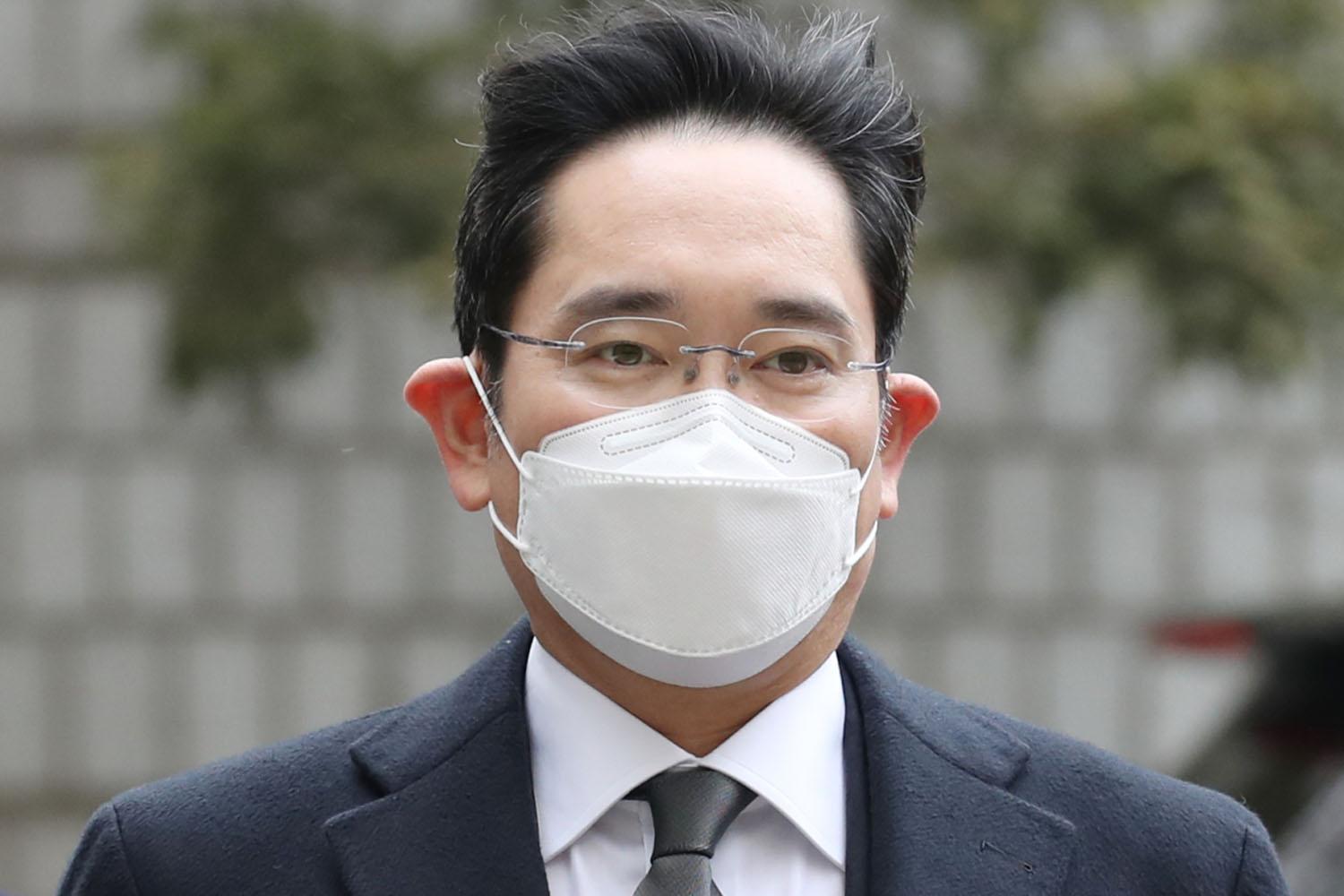 ชายสวมชุดสูทเดินในพื้นที่กลางแจ้ง โดยมีพื้นหลังเป็นทางเดินอิฐ