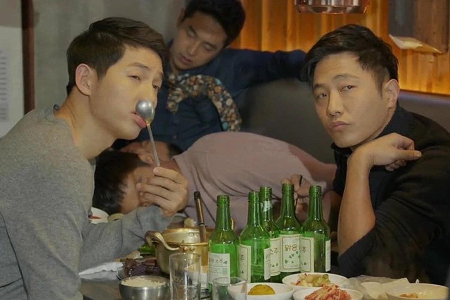 一羣人在餐廳共享韓國餐點,桌上擺滿了韓國燒酒和各式配菜,體現用餐分享氛圍。