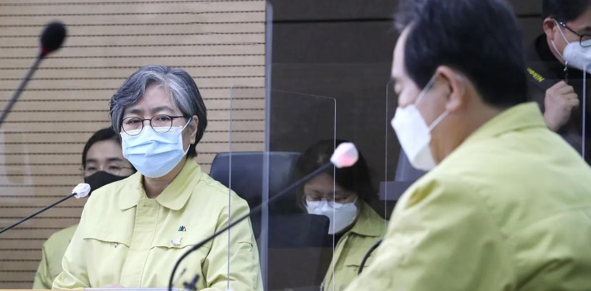 บุคคลสวมเสื้อสีเหลืองพูดในการประชุมแถลงข่าวในเกาหลีเกี่ยวกับการจัดการทรัพยากรช่วงวิกฤติเเพร่ระบาดของไวรัสโควิด-19 ภาพมีพื้นหลังไม้และไมโครโฟนหลายอันวางอยู่บนโต๊ะในการแถลงข่าวที่จัดขึ้นในเกาหลี สิงหาคม 2020 ที่ผ่านมา