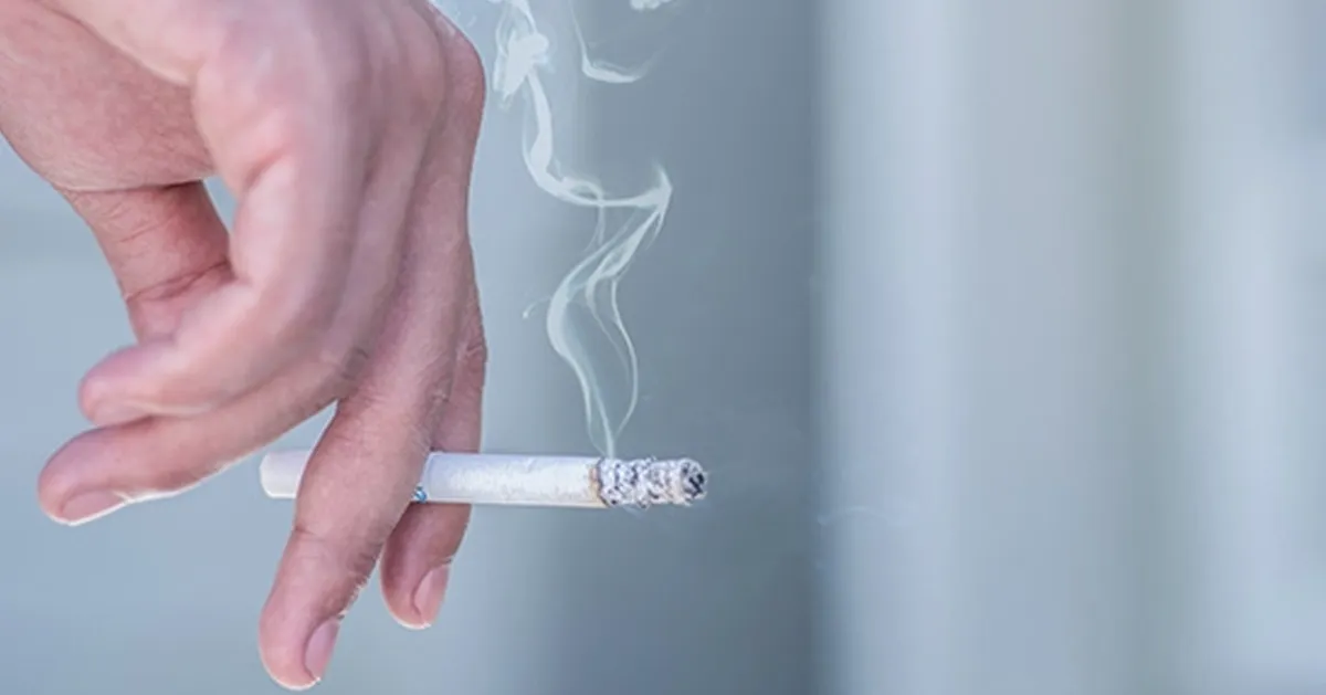 มือที่ถือบุหรี่กำลังไหม้และมีควันล่องลอย