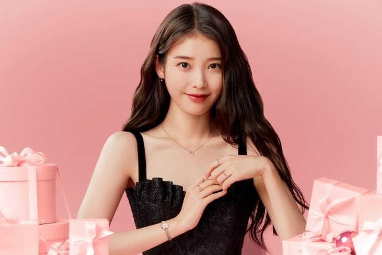 韓國著名歌手 IU 身穿黑色禮服，周圍環繞著粉紅色的禮物盒，在淡粉色背景下擺出優雅姿態。「Creatrip」提供