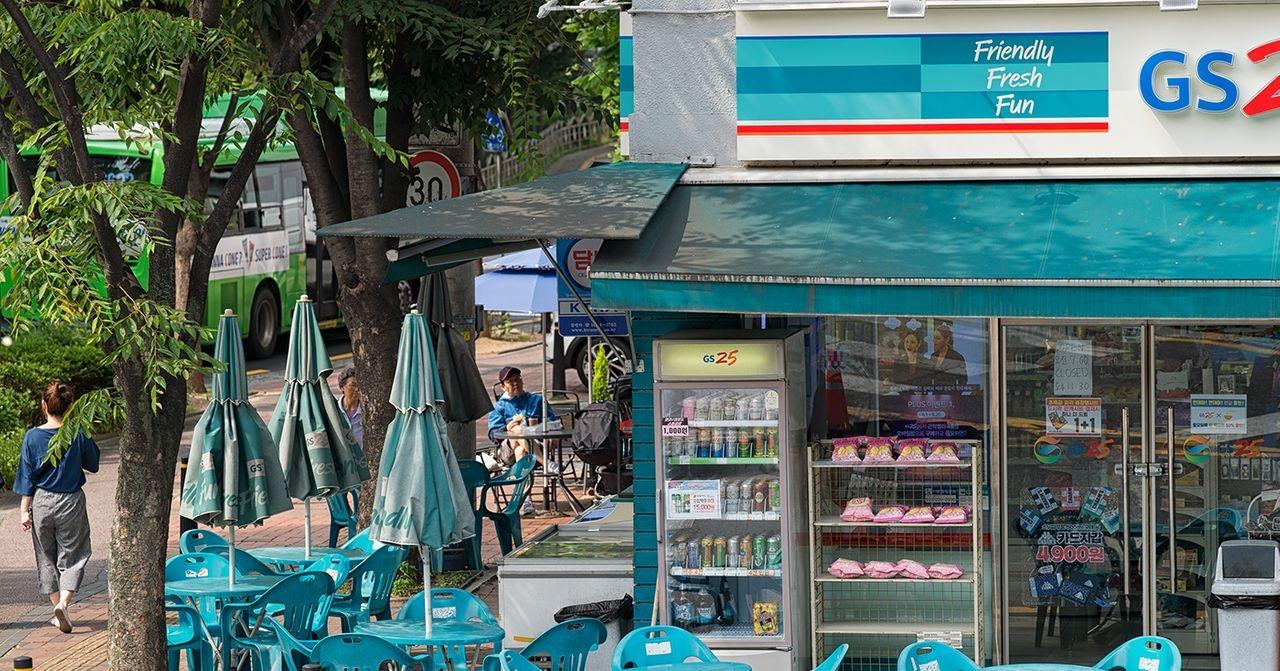 ด้านหน้าร้านสะดวกซื้อ GS25 ในเกาหลีพร้อมโต๊ะและเก้าอี้สำหรับนั่งพักผ่อน สภาพแวดล้อมที่สะดวกสบายและเป็นมิตรสำหรับผู้ที่ผ่านไปมา