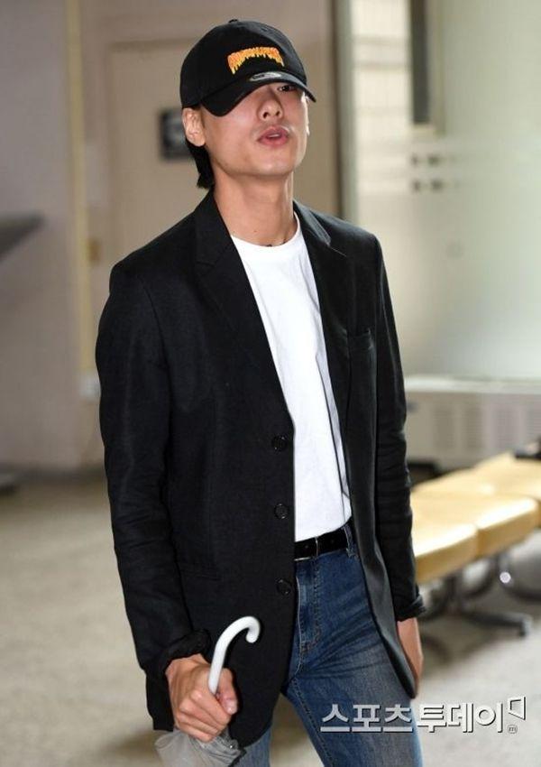 アイアン、カジュアルなネイビーのブレザーとデニム、白いTシャツを着ている場面。手にはビニール袋と傘を持っている