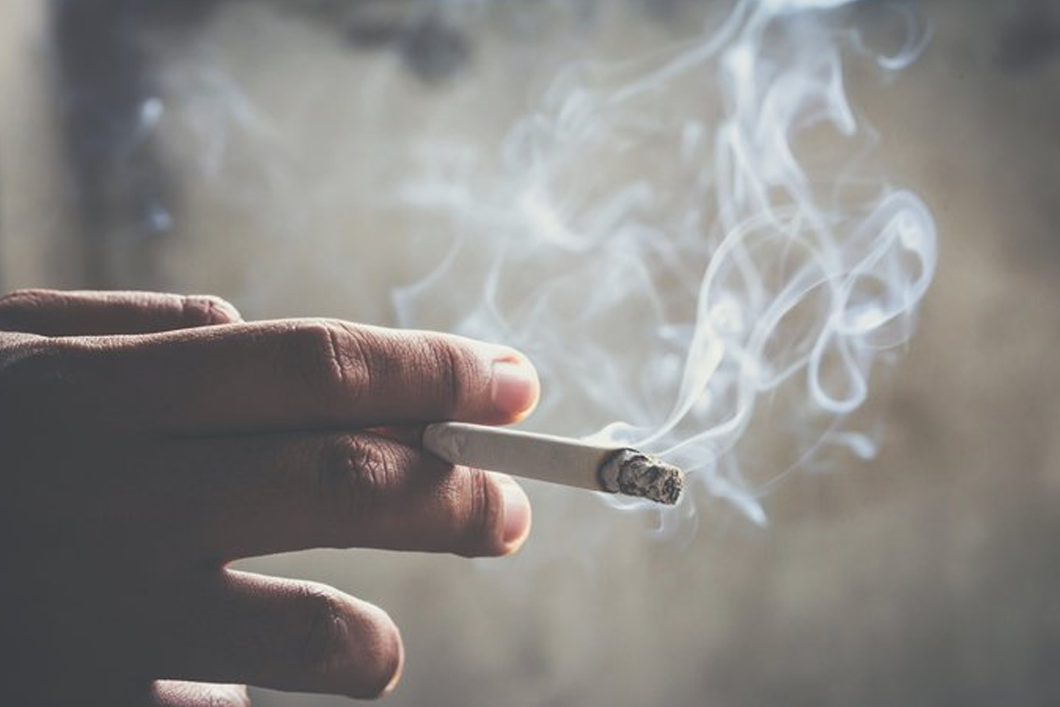 手中夹着燃烧的香烟，烟雾在空气中弥漫，韩国即将提高香烟价格以改善健康。