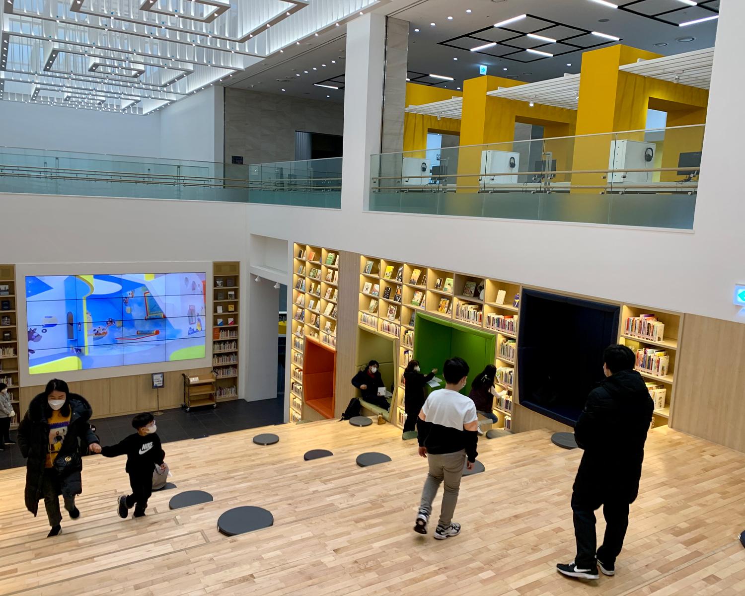 Menschen stöbern in der Haupthalle des Songpa Buchmuseums, umgeben von einer warmen, einladenden Atmosphäre mit hölzernem Design.