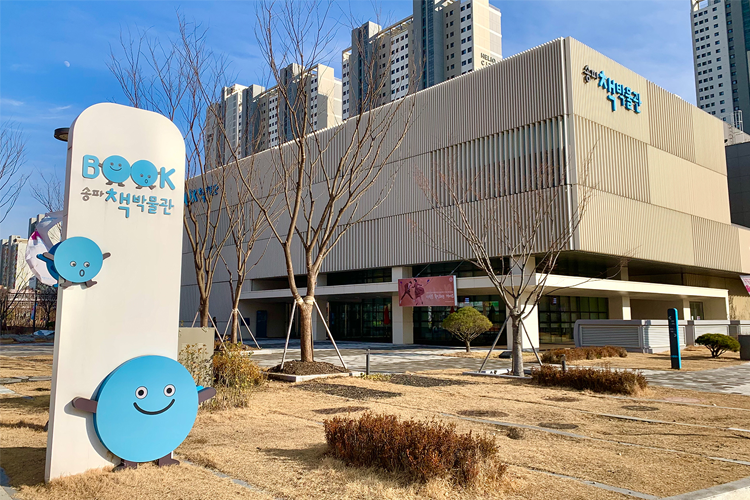 松坡“书的博物馆”外观，展示现代建筑设计，周围是高耸的公寓楼，整体环境和谐美观。