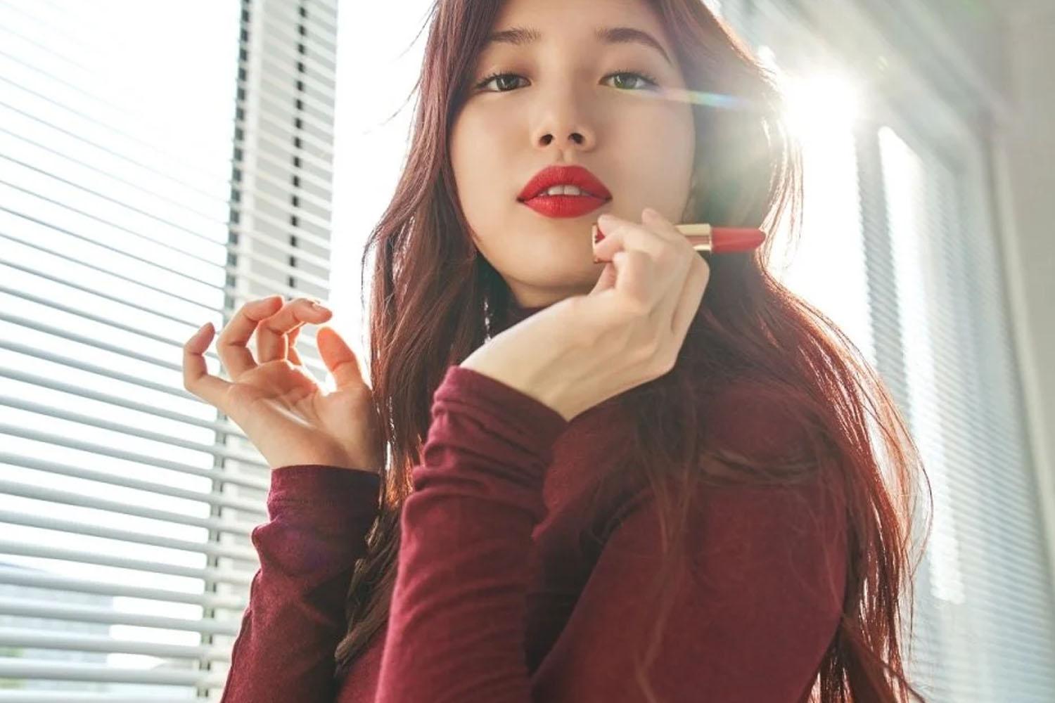 ภาพหญิงสาวใช้ลิปสติกสีแดงในห้องที่มีแสงส่องเข้ามาทางหน้าต่าง