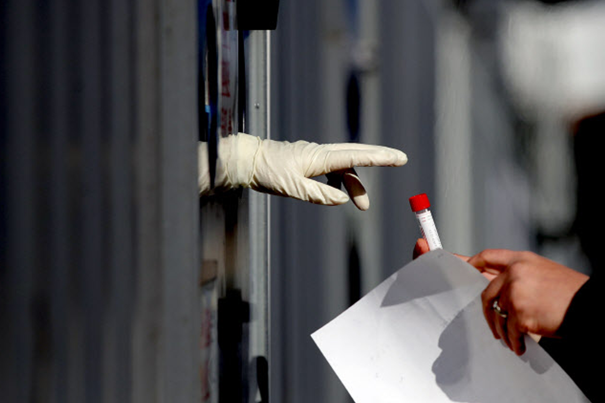 在韓國檢測隊伍中，工作人員戴著防護手套正在接收一個樣本管，強調防疫措施的重要性。