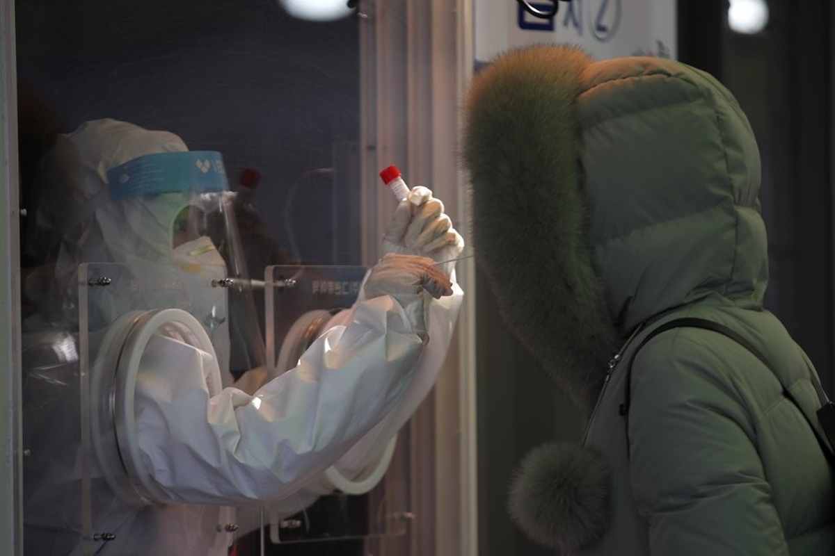 防疫工作者在檢測窗口內，與一位穿著厚外套的市民進行樣本交換，背景顯示嚴格的防疫程序。