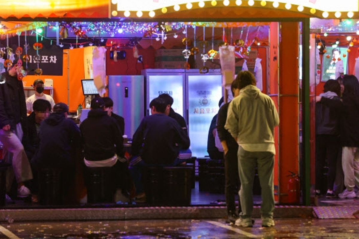 首爾建大附近的酒吧夜間外觀，一羣年輕人正在户外等候進入，酒吧內部燈光絢爛，反映華燈初上的氣氛。
