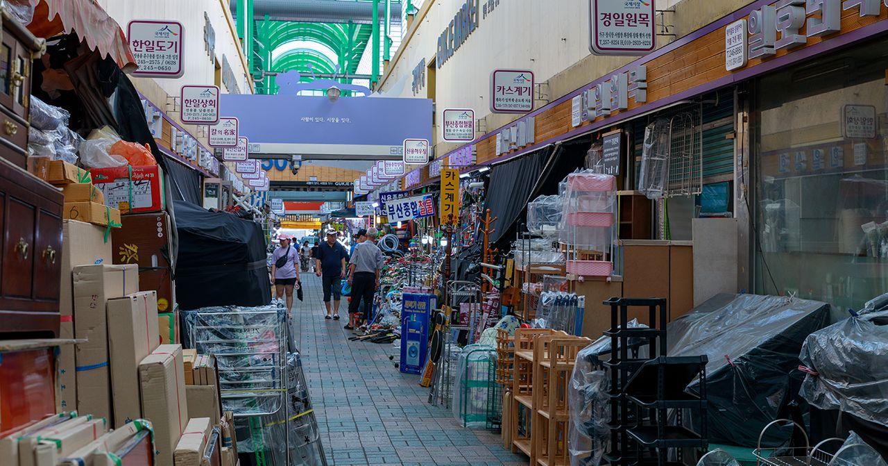 Daytime at Bupyeong Market in Busan, with stalls selling a variety of household items and goods under clear Korean signage.