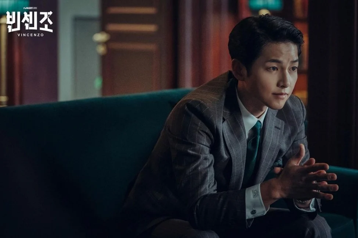 Song Joong-ki sitting down with his hands together in a grey suit on new K-drama Vincenzo
