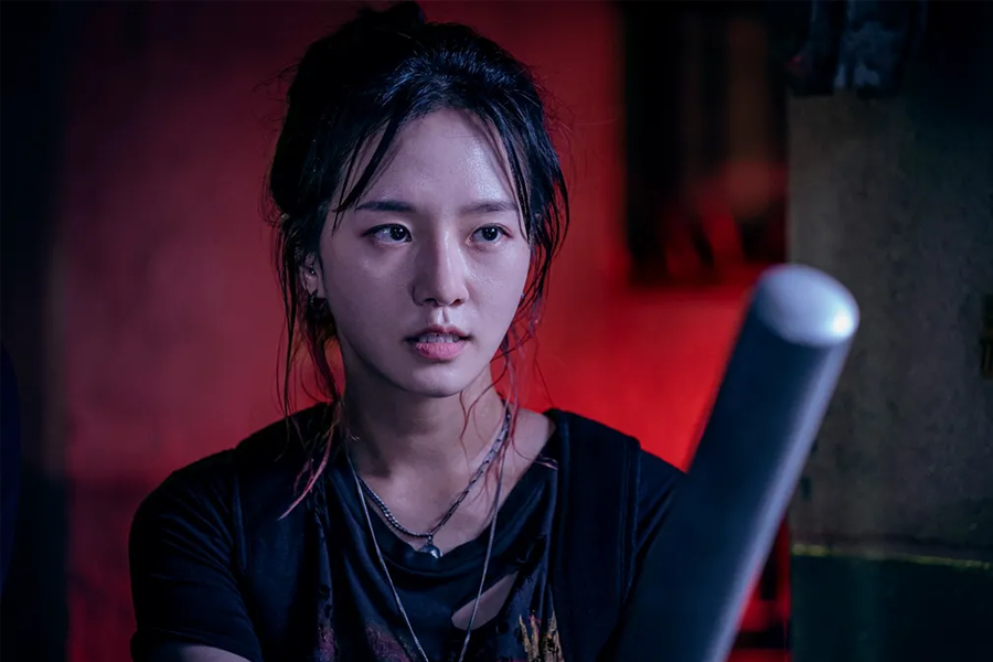 韓國電視劇《Sweet Home》中一位角色手握棍棒,背景呈現出紅色的燈光效果,使場景充滿緊迫感,來自Netflix的圖片。