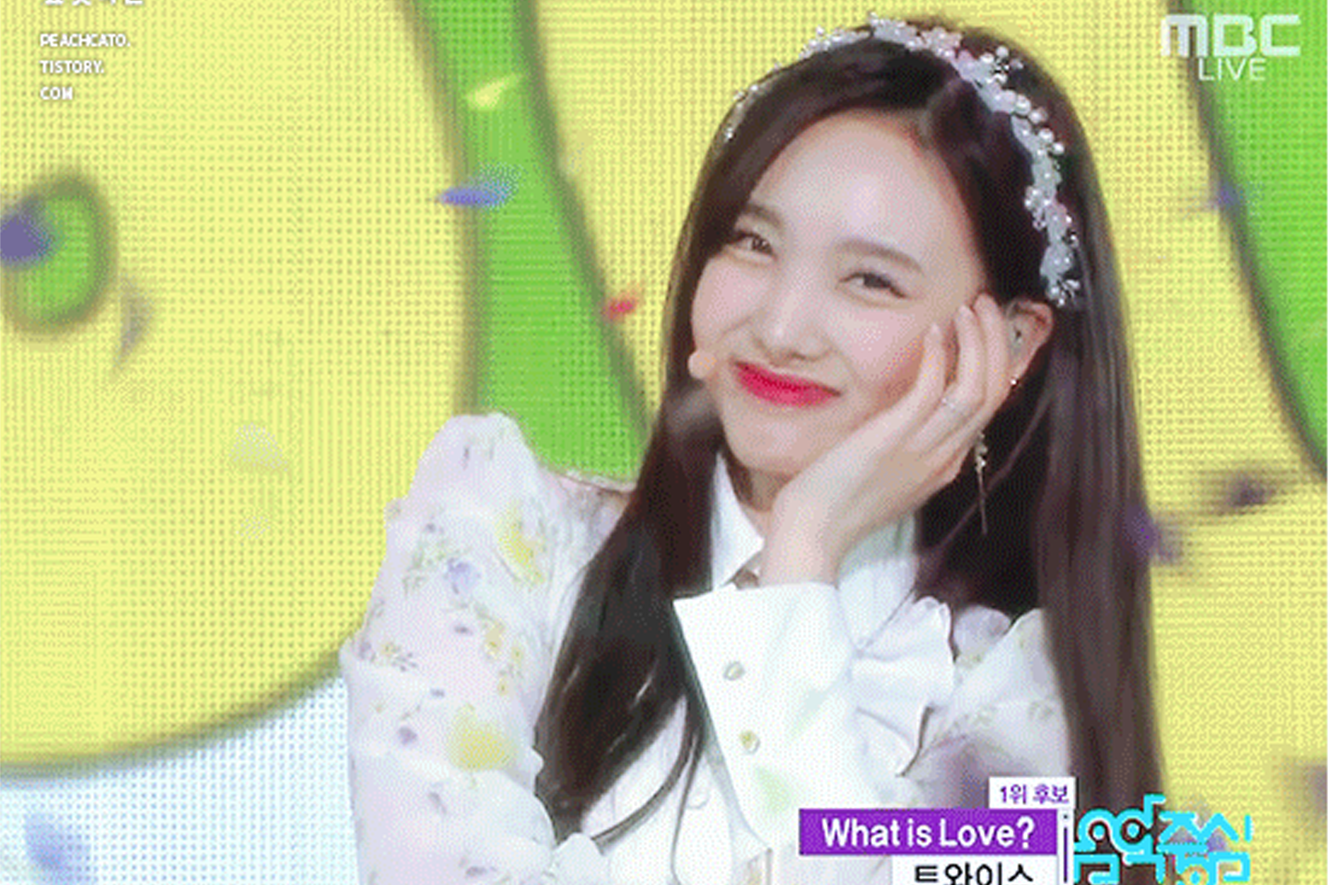 TWICE - 娜璉 在音樂節目畫面中，以白色裝扮演出。