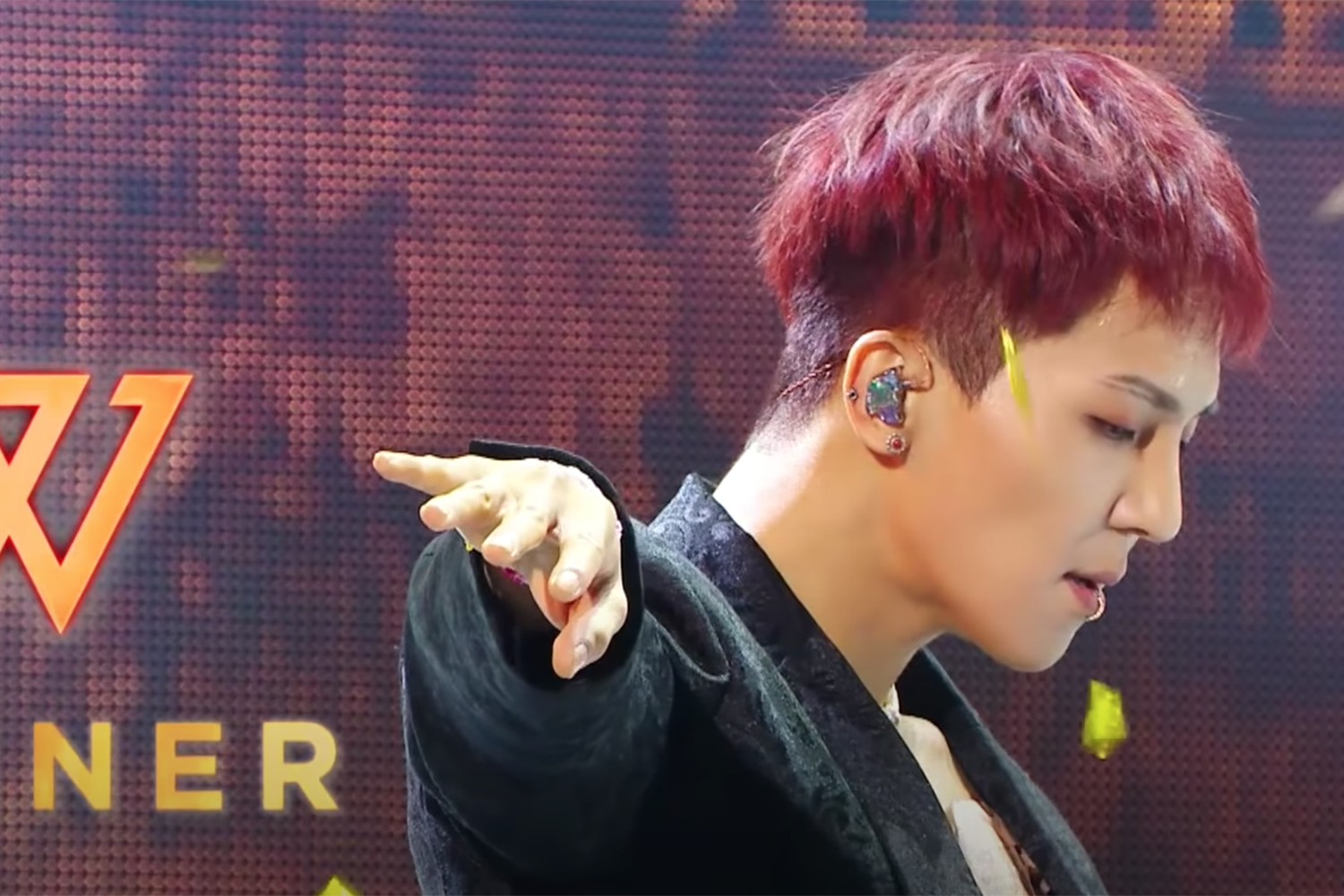 ภาพสมาชิกวง Winner ซง มิโน ขณะกำลังแสดงบนเวที ด้วยท่าทางที่น่าดึงดูดและผมสีแดงที่โดดเด่น