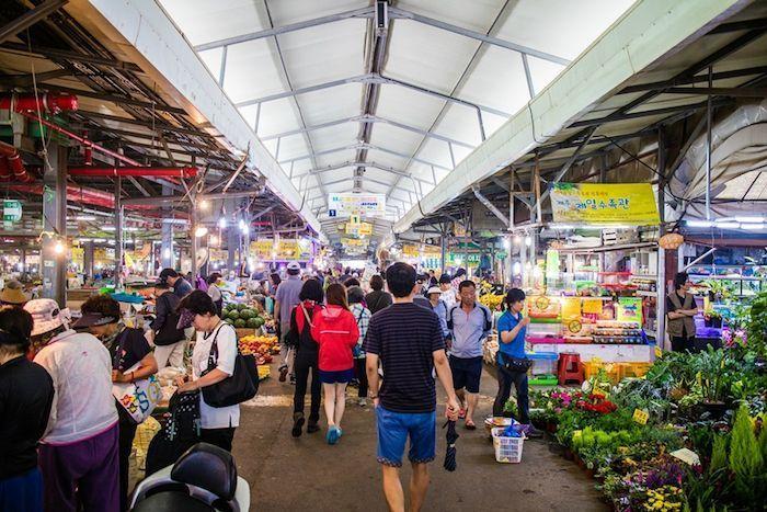Inside view of a bustling Korean 5-day market with people shopping for fresh produce and other goods, showcasing the vibrant market atmosphere.