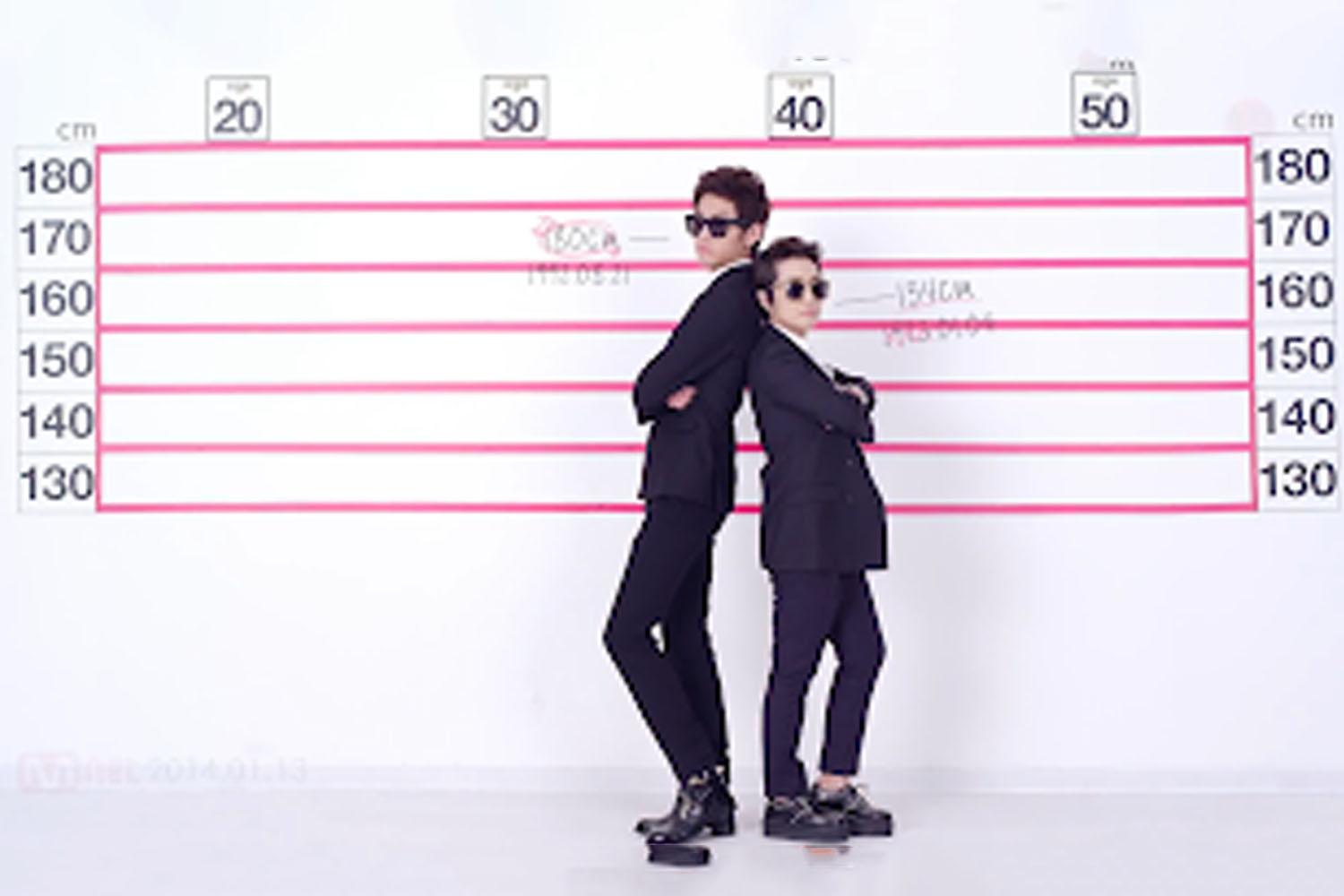 韓國男性穿著黑色西裝對比身高背景板，體現韓國男子平均身高的高低差。