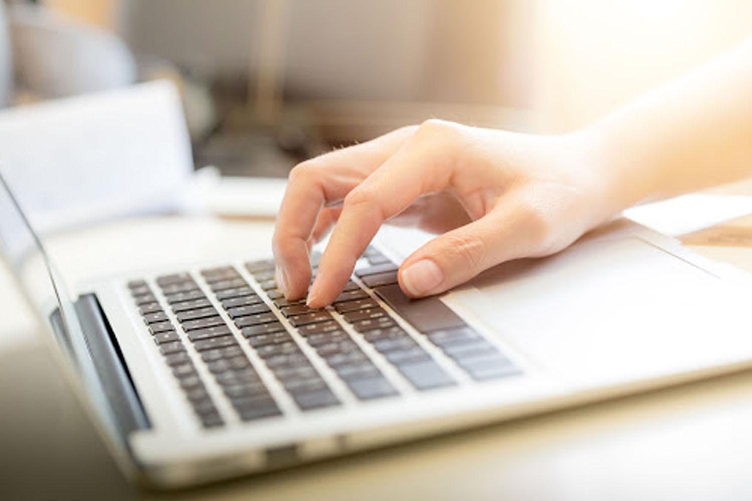 มือที่กำลังพิมพ์บนแล็ปท็อป ซึ่งอาจเกี่ยวข้องกับการทำงานออนไลน์หรือการทำงานจากที่บ้านในช่วงโควิด-19