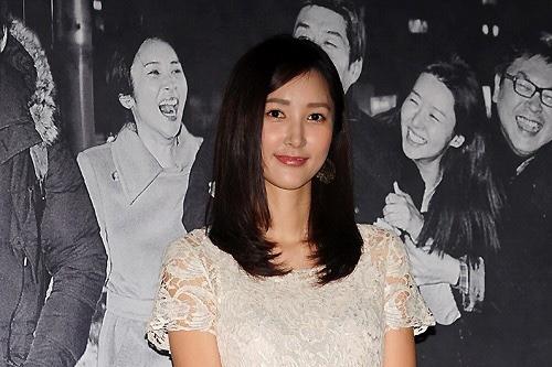 白いレースのドレスを着た人物の上半身の写真。背景には人々が写っているが顔はぼかされている。