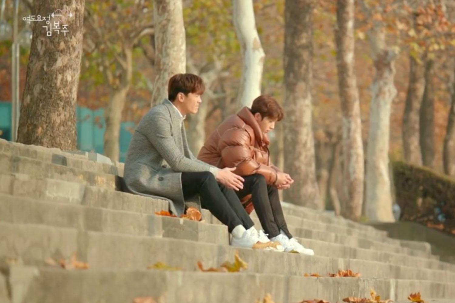 บรรยากาศฤดูใบไม้ร่วงที่มหาวิทยาลัยในเกาหลี นักศึกษาสองคนกำลังนั่งคุยกันบนบันไดที่มีใบไม้ร่วงอยู่โดยรอบ