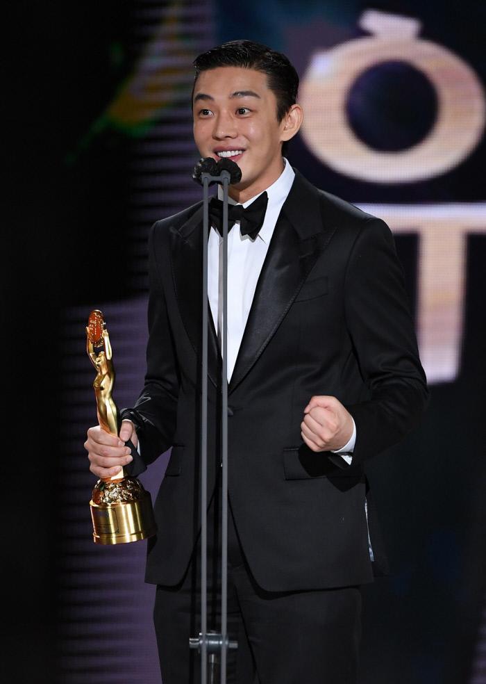 第41回青竜映画賞の授賞式で主演男優賞を受賞し、喜びを噛みしめる俳優。タキシード姿でトロフィーを抱え、誇らしさを表現している。