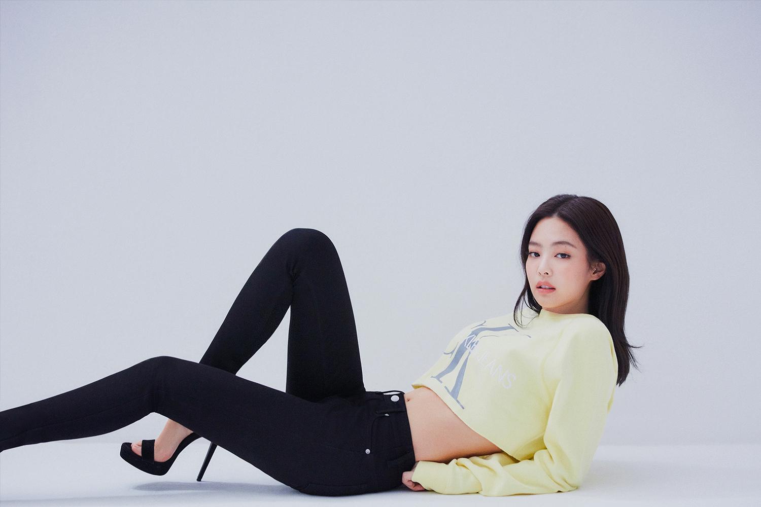 Celebrità coreana con un maglione giallo e pantaloni neri in posa in un studio fotografico.