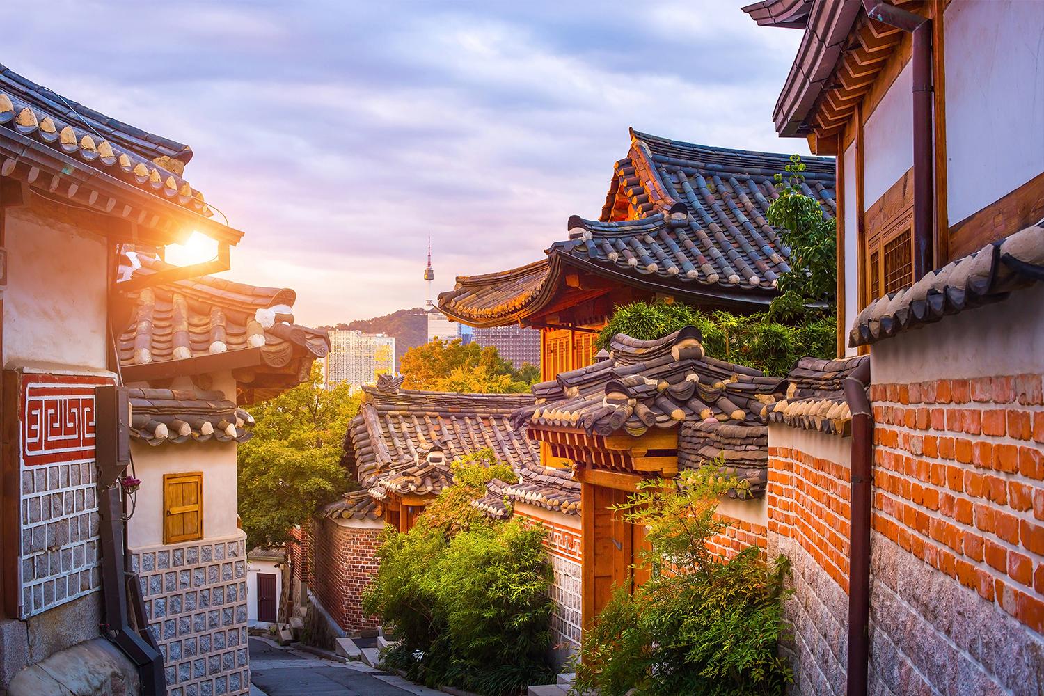 Vista del Villaggio Hanok di Bukchon a Seoul, con tradizionali case coreane sotto un cielo colorato al tramonto.