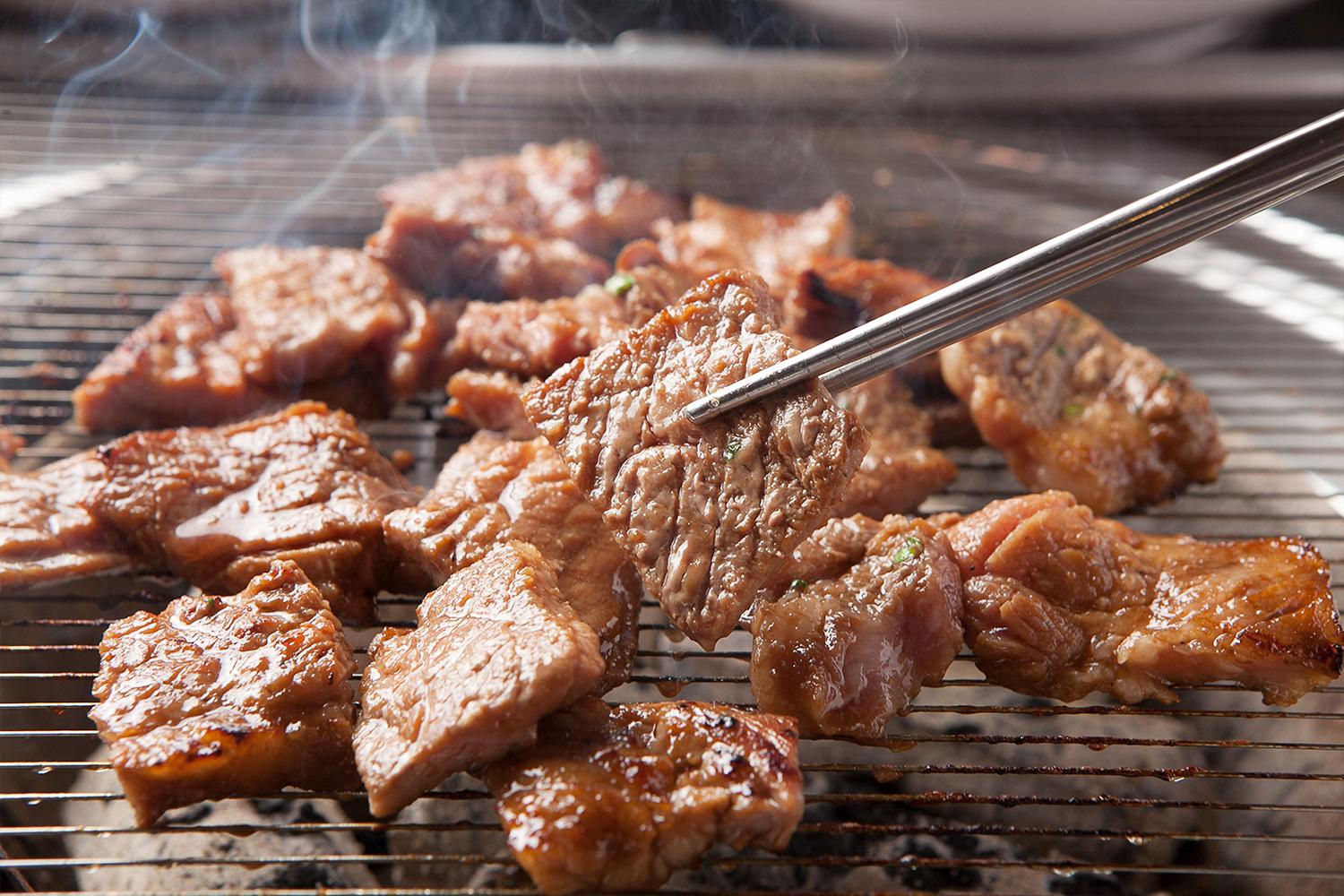 Carne di maiale marinata che viene grigliata su una griglia con paio di bacchette in acciaio.