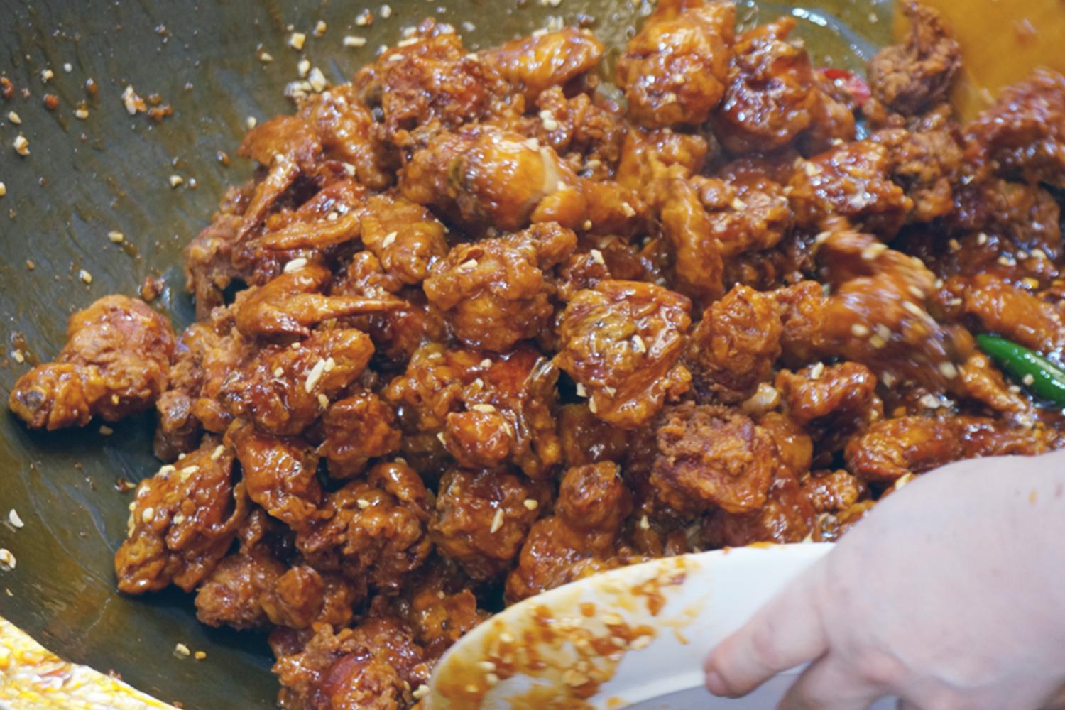 Close-up view of Dakgangjeong, the sweet and crispy Korean fried chicken dish, being stirred in a large pan, popular in Incheon.