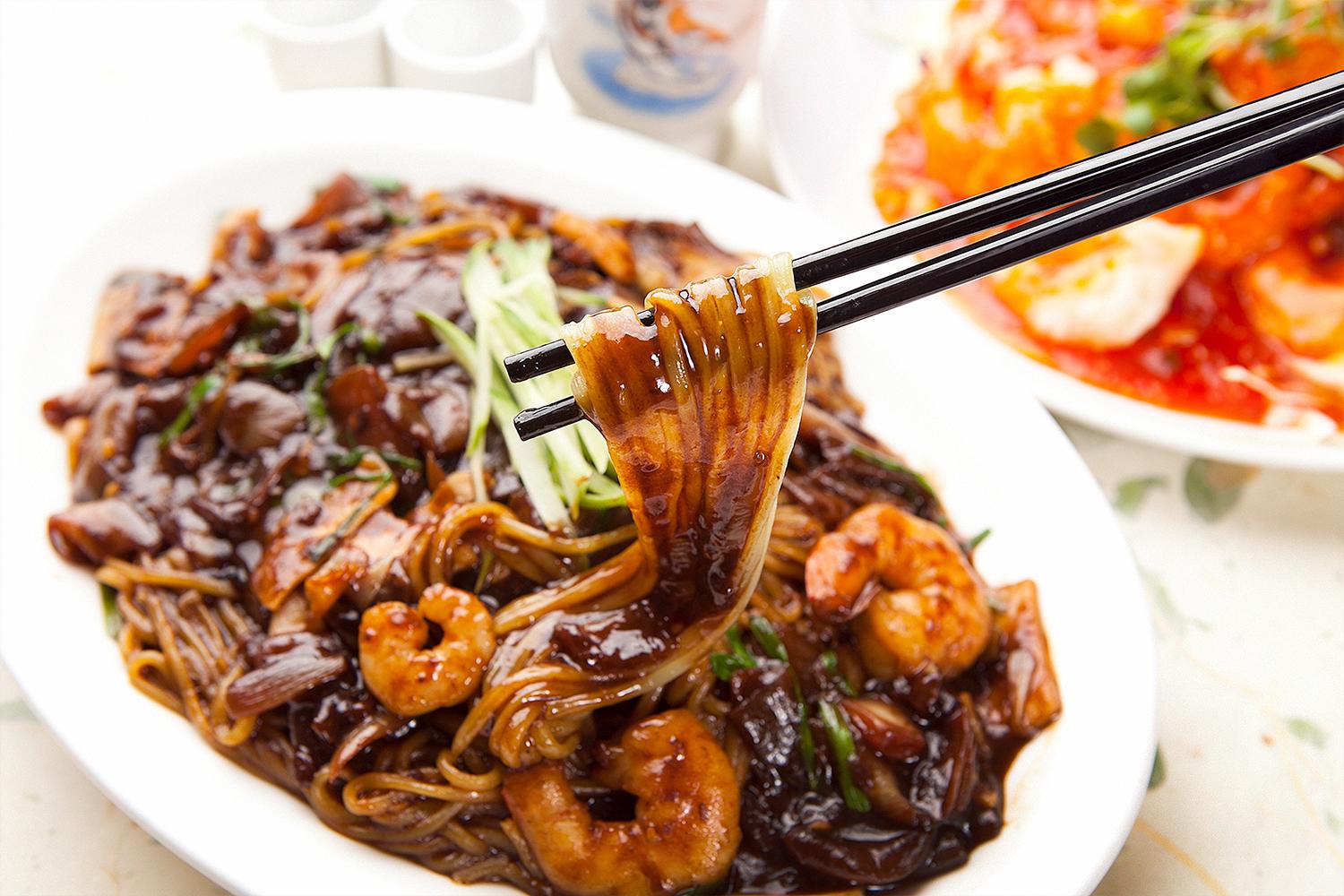 Close-up of Jjajangmyeon, black bean noodles topped with julienned cucumbers and shrimp, a beloved dish in Incheon.