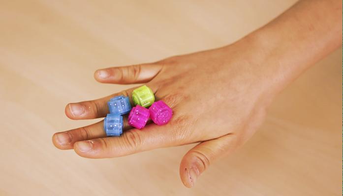 มือของคนที่กำลังถือหมากคงกีหลากสีหลายชิ้นเพื่อเตรียมเล่นเกมคงกีโนรี เกมที่เป็นที่นิยมในวัยเด็กสำหรับเด็กผู้หญิงในเกาหลี พื้นหลังเป็นไม้สีน้ำตาลอ่อน สร้างบรรยากาศการเล่นเกมในบ้านอย่างอบอุ่น