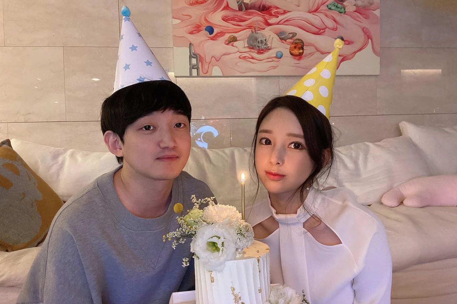 兩位身穿簡約服飾的男女在熱鬧的生日派對上面, 戴著可愛的紙製生日帽, 臉上洋溢著幸福。二人共同切著裝飾有鮮花的漂亮生日蛋糕。