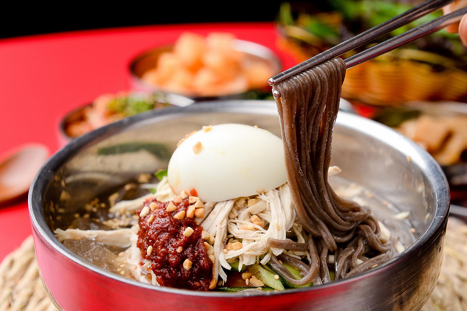 Makguksu, hidangan mie soba dingin Korea, disajikan dengan telur dan bumbu pedas.