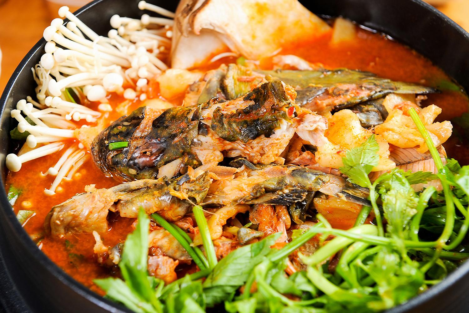 Minmul Maeun-tang, sup ikan air tawar pedas Korea, ditampilkan dengan ikan dan jamur di atas meja.