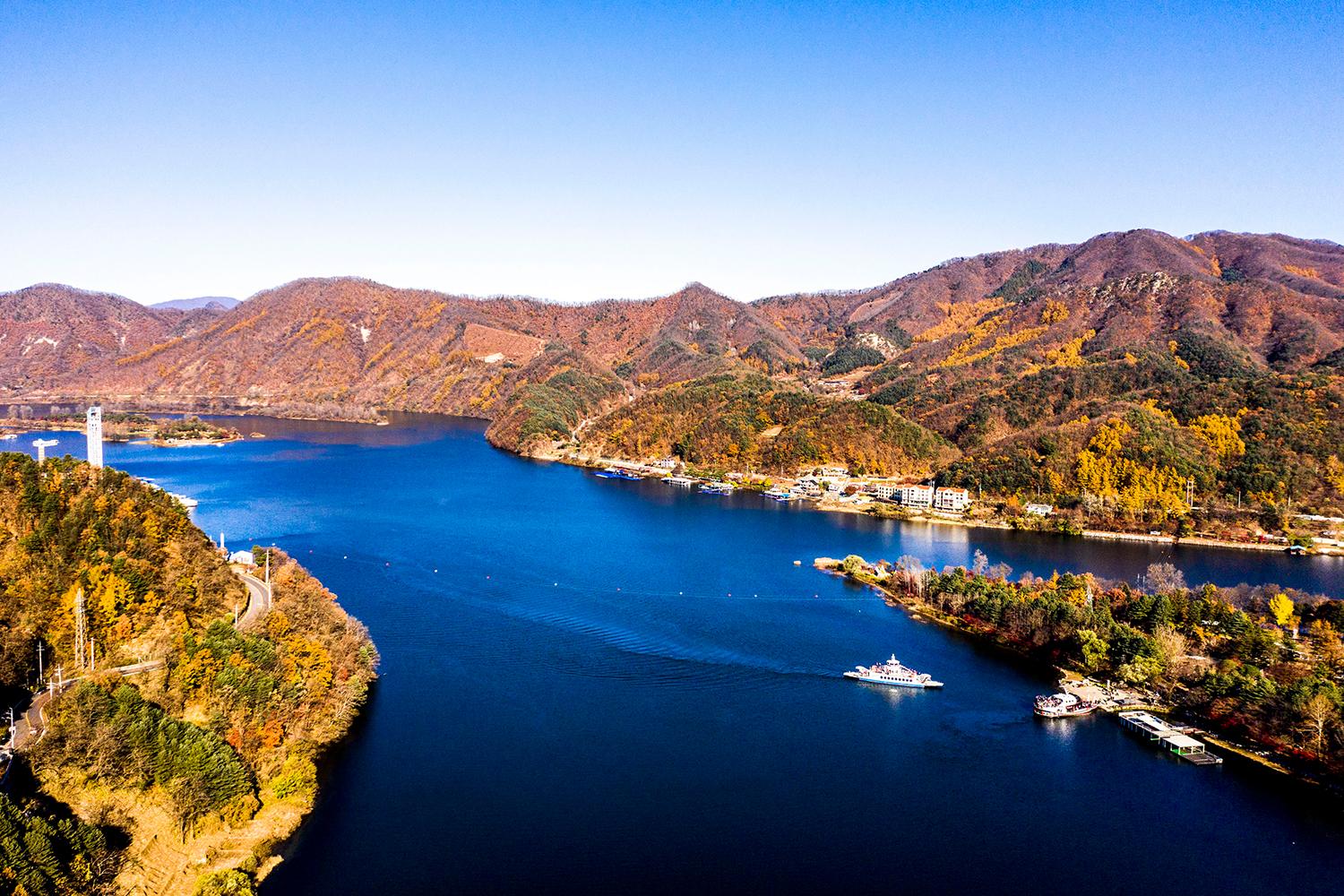 Pemandangan indah Pulau Nami di Korea Selatan dengan air biru dan pegunungan yang dipenuhi pepohonan.
