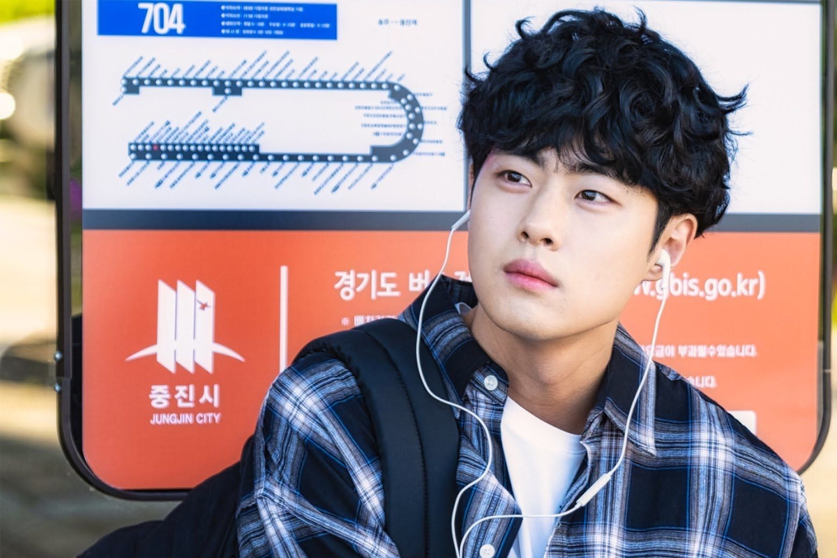 电视剧《驱魔面馆》中赵炳圭的角色形象，坐在公共交通站点，身穿便装并戴着耳机，表现出角色的日常生活一面。