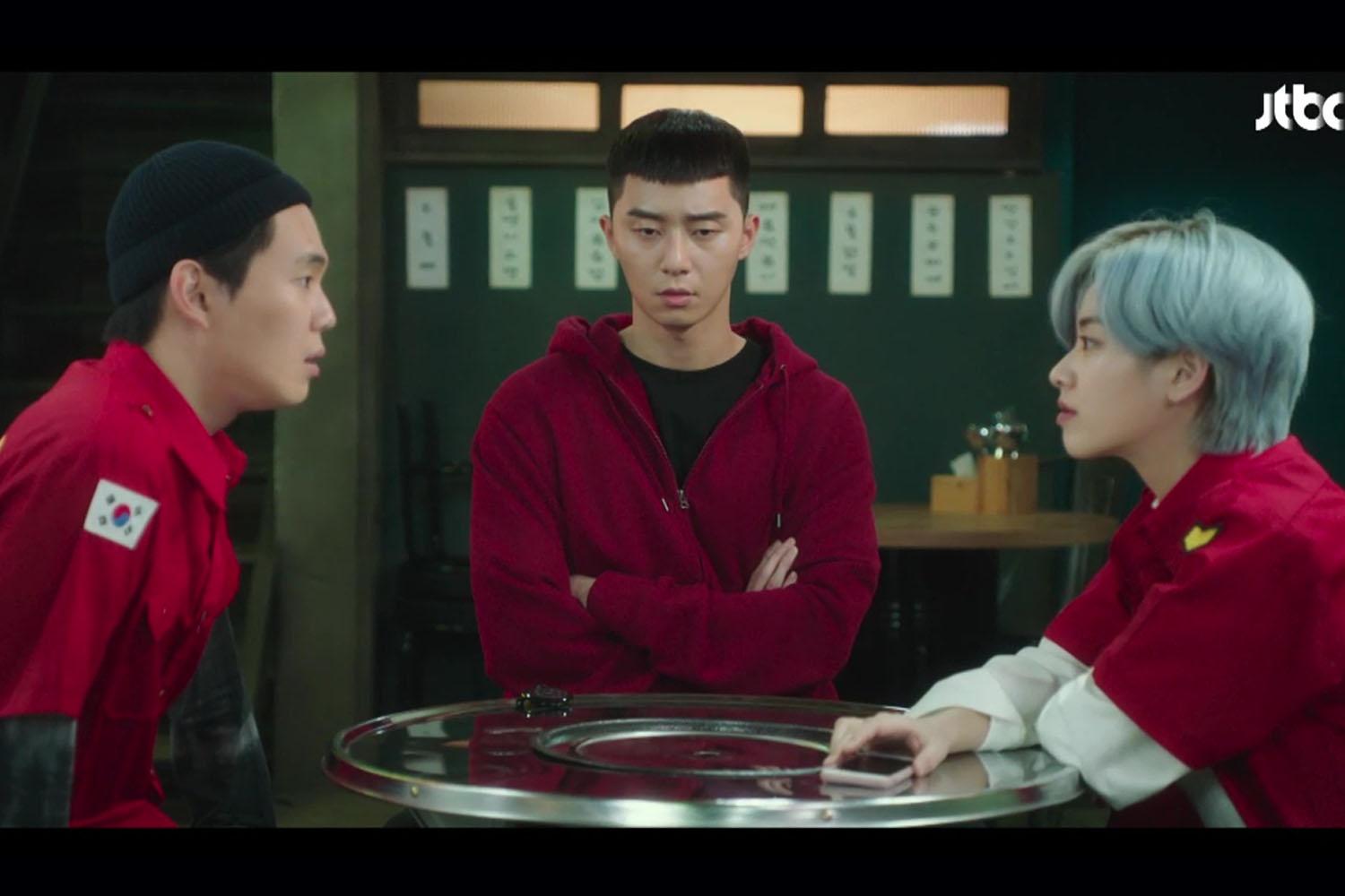 三位角色在韓國電視劇拍攝場景中坐在圓桌旁，展示韓國工資法影響工作時間的情況。