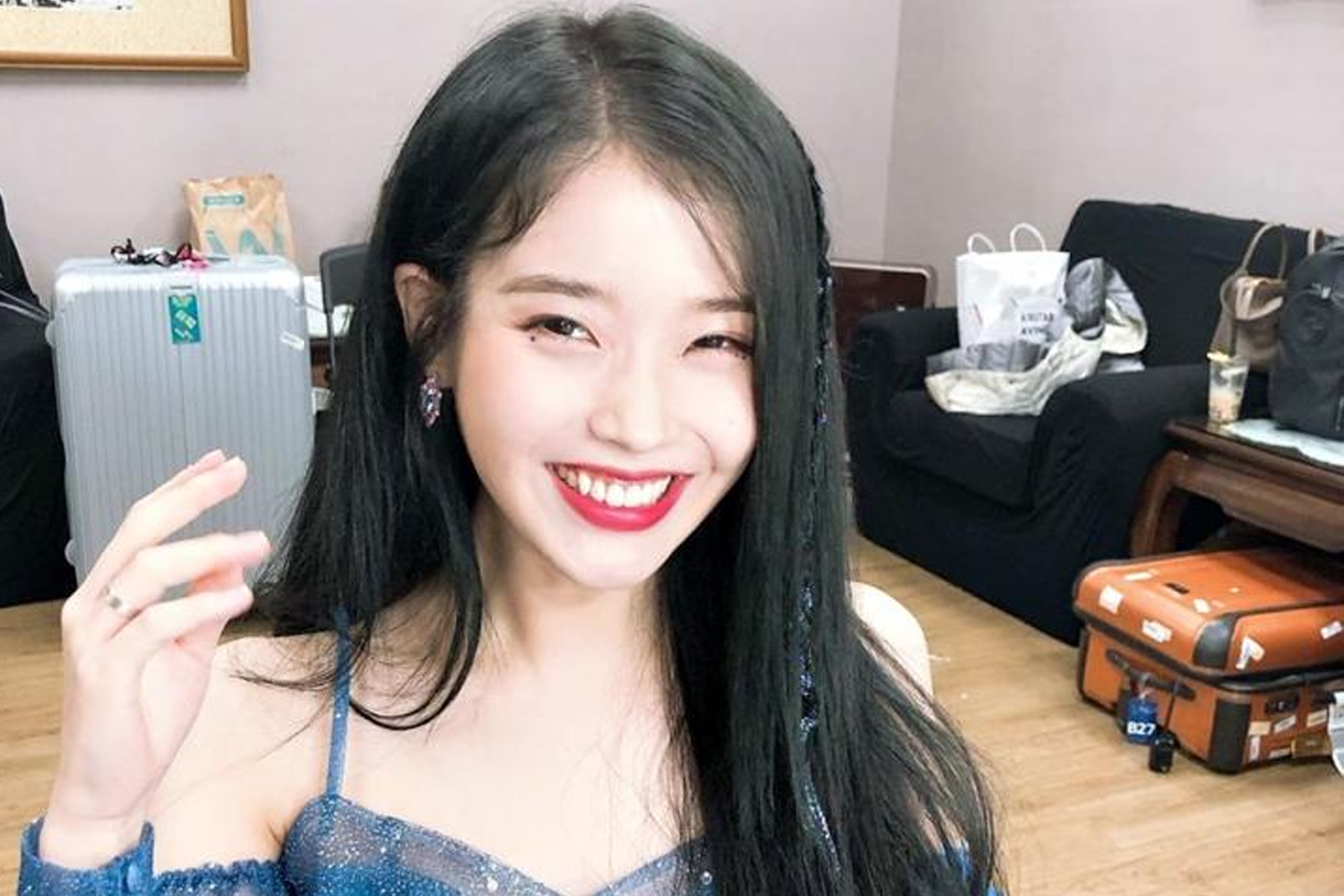 IU身穿精緻藍色舞台服裝，背景為化妝間，地上有許多旅行箱和揹包。