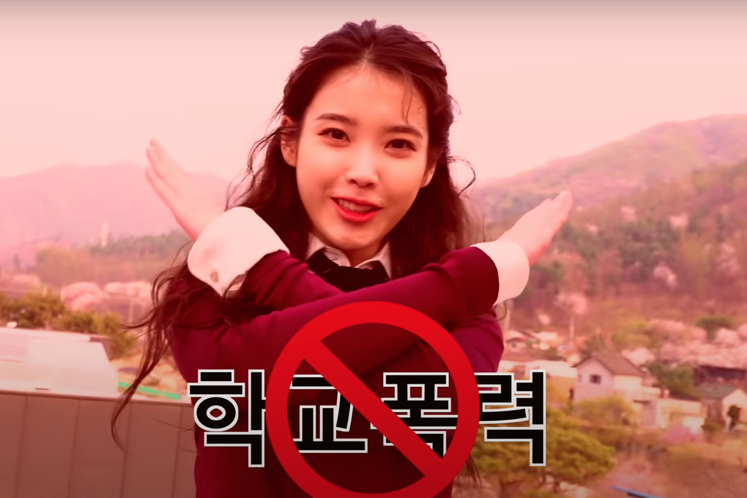 IU身穿校服,雙臂交叉顯示抵制校園暴力,背景為紅色調教學樓和景觀。韓文字幕指向校園暴力話題。