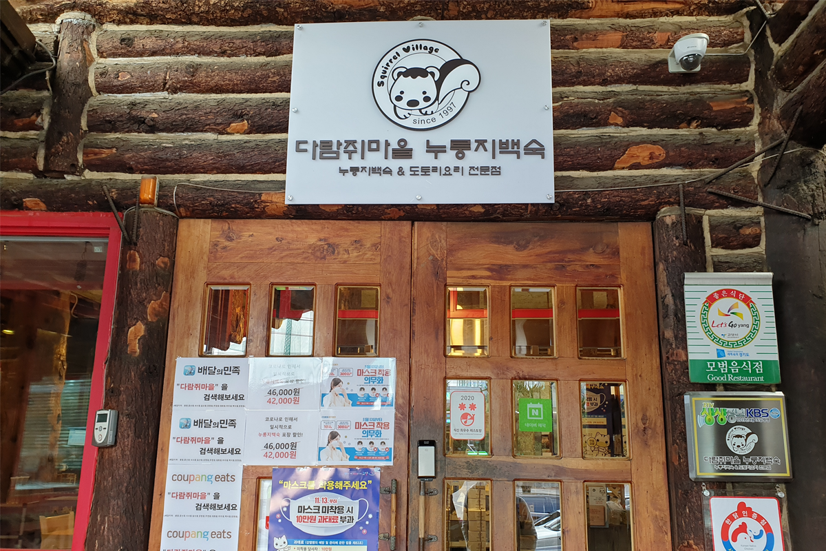 다람쥐 마을 누룽지백숙 레스토랑의 입구 사진으로, 간판과 다양한 안내 포스터들이 붙어 있습니다.