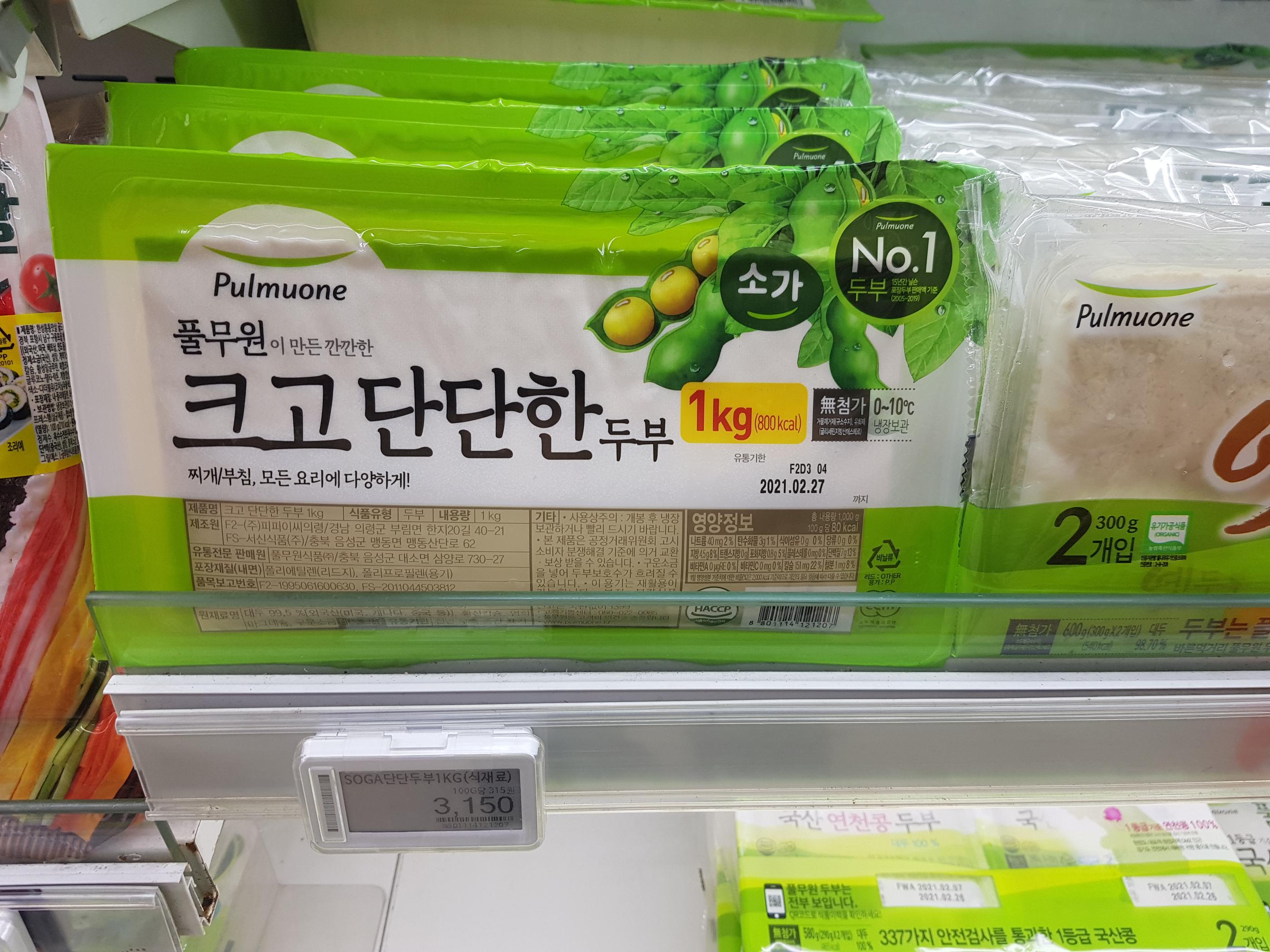 韓国のスーパーマーケットの豆腐コーナーで、1キログラムの豆腐が並んでいる画像です。大きくてしっかりとした豆腐が強調され、健康志向や韓国の食文化を感じさせる一枚です。