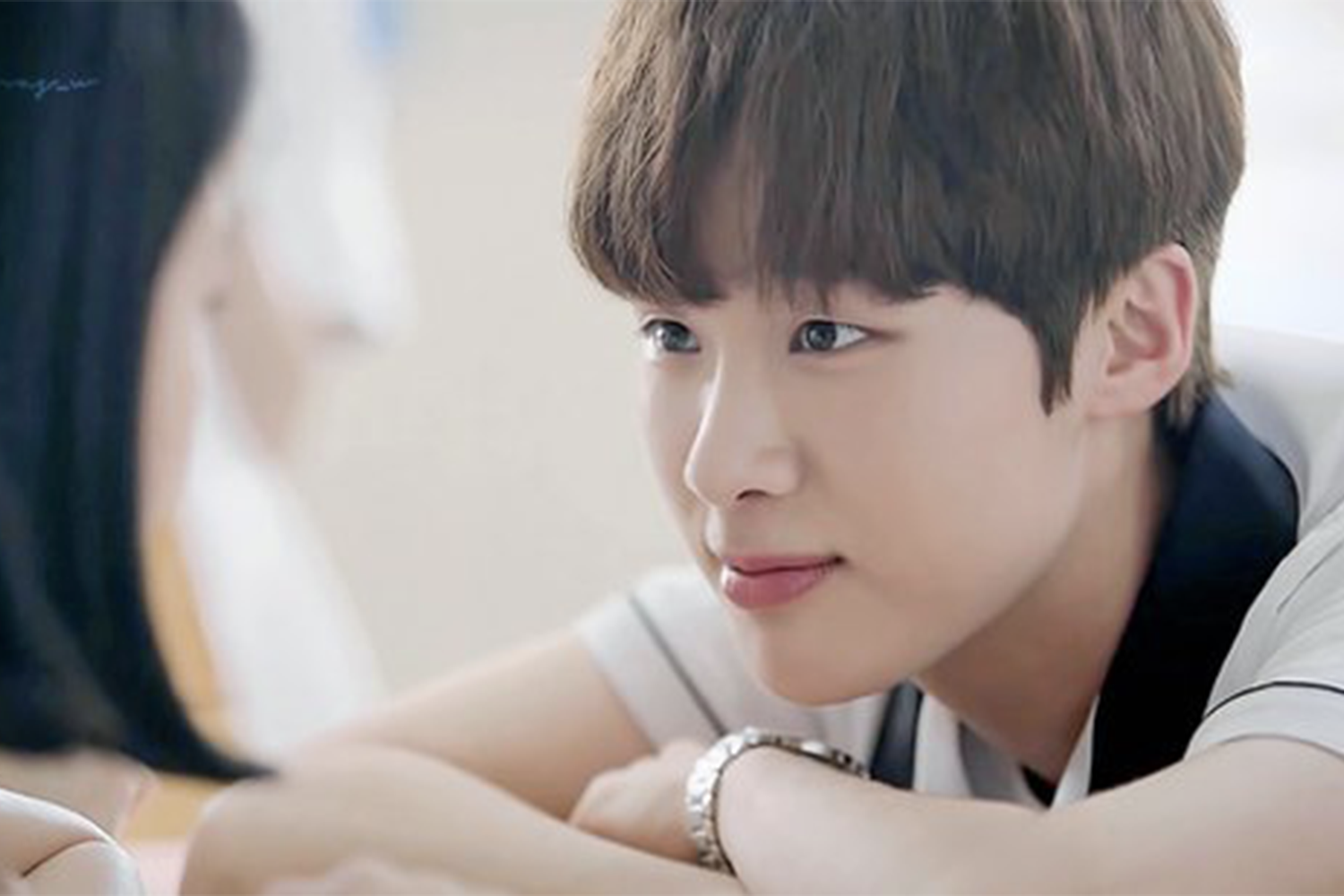 韓國校園劇情場景，一位男學生穿著校服在課堂上與同學交談。