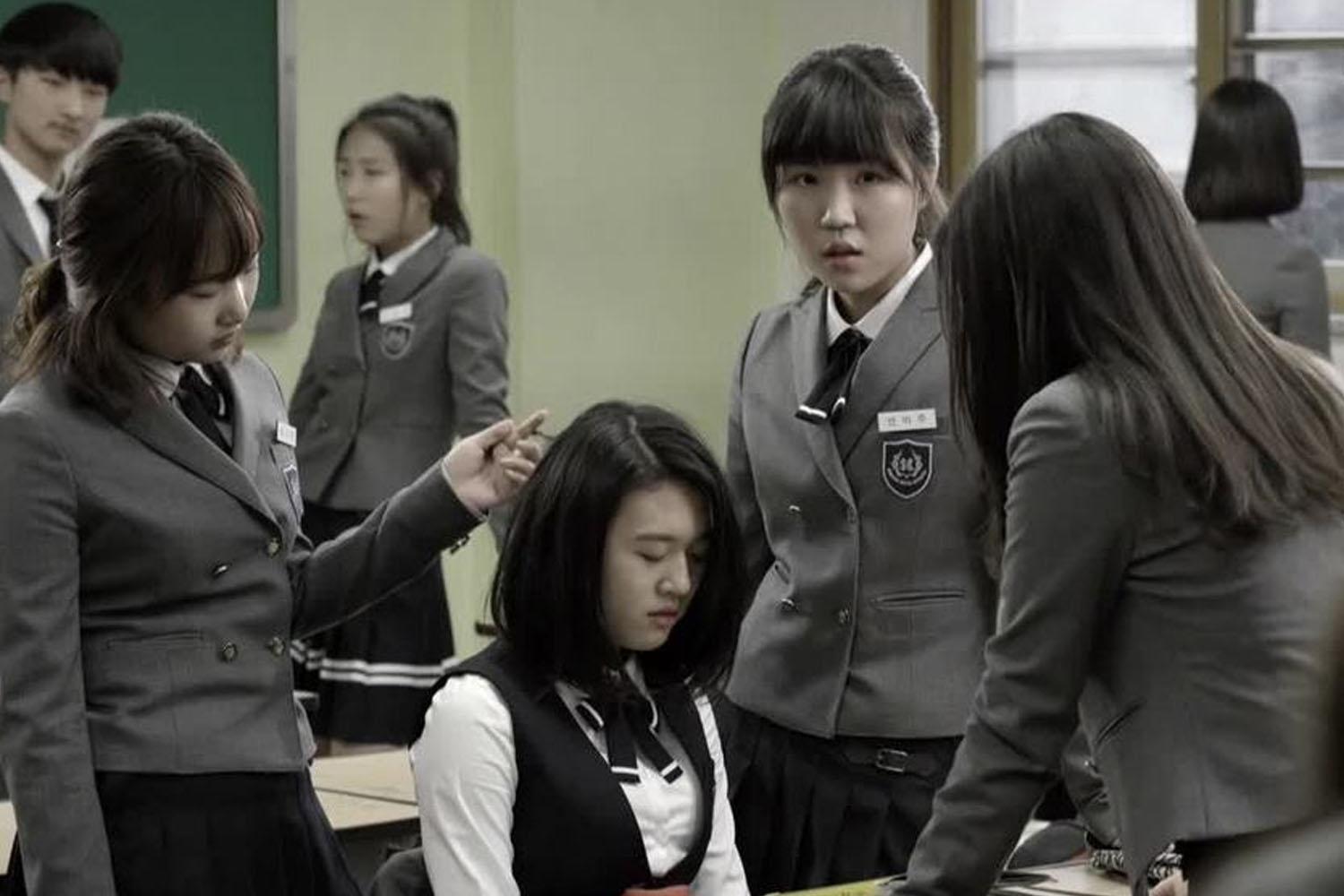 นักเรียนหญิงในห้องเรียนยืนล้อมรอบหญิงสาวคนหนึ่งที่ดูเหมือนจะตกเป็นเป้าหมาย แสดงถึงสถานการณ์การกลั่นแกล้งในโรงเรียนของเกาหลีใต้