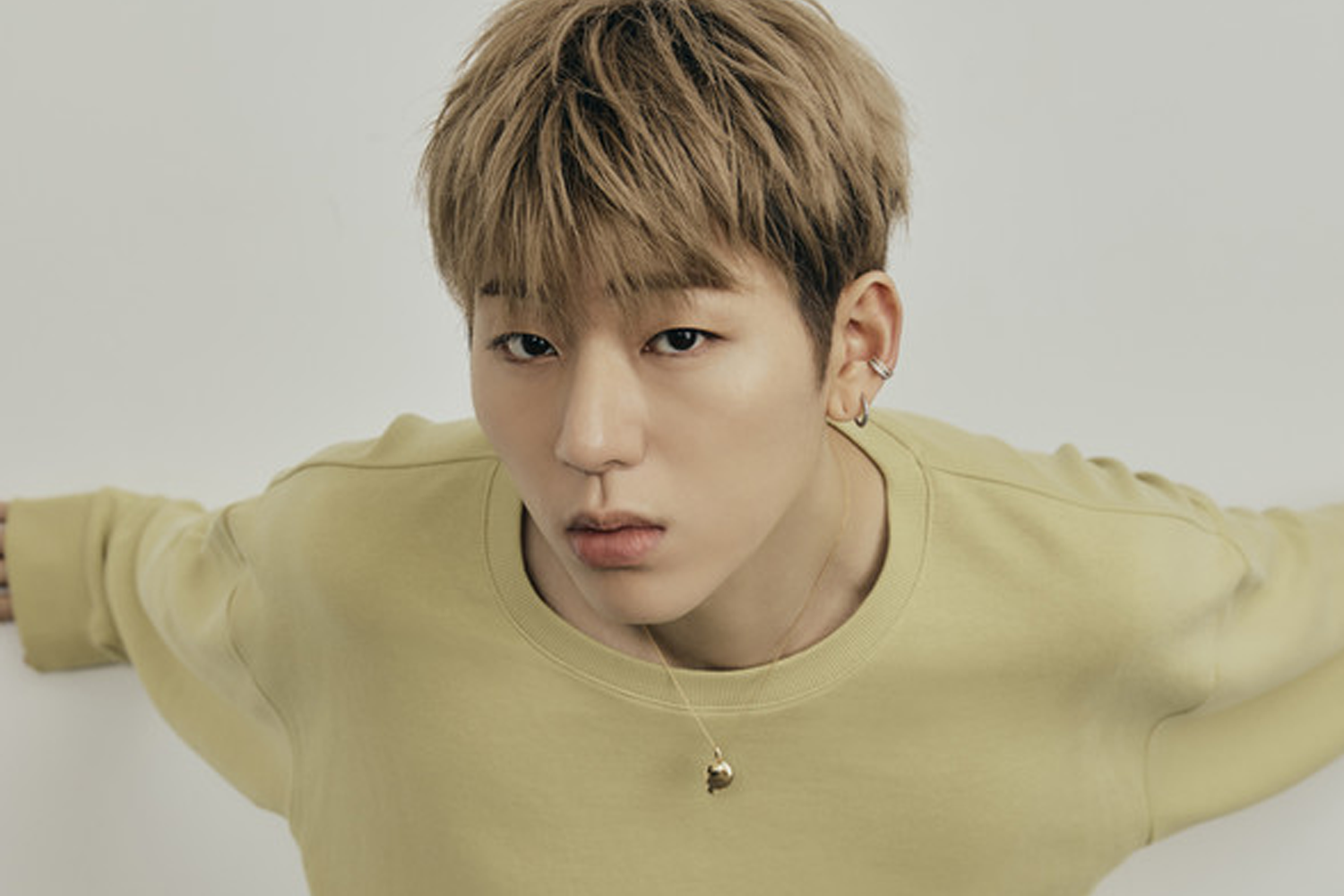 Zico 穿著淡黃色上衣，雙臂展開，背景為淺白色。