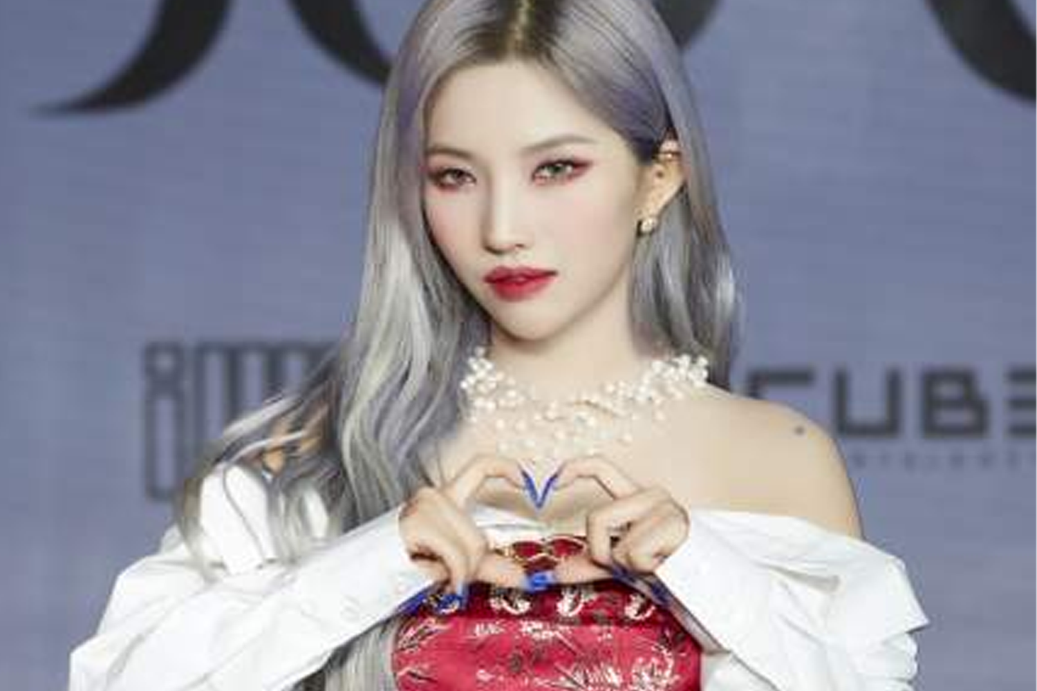 (G)I-DLE 成員小娟在舞台背景前，穿著紅色禮服並用手做心形手勢。