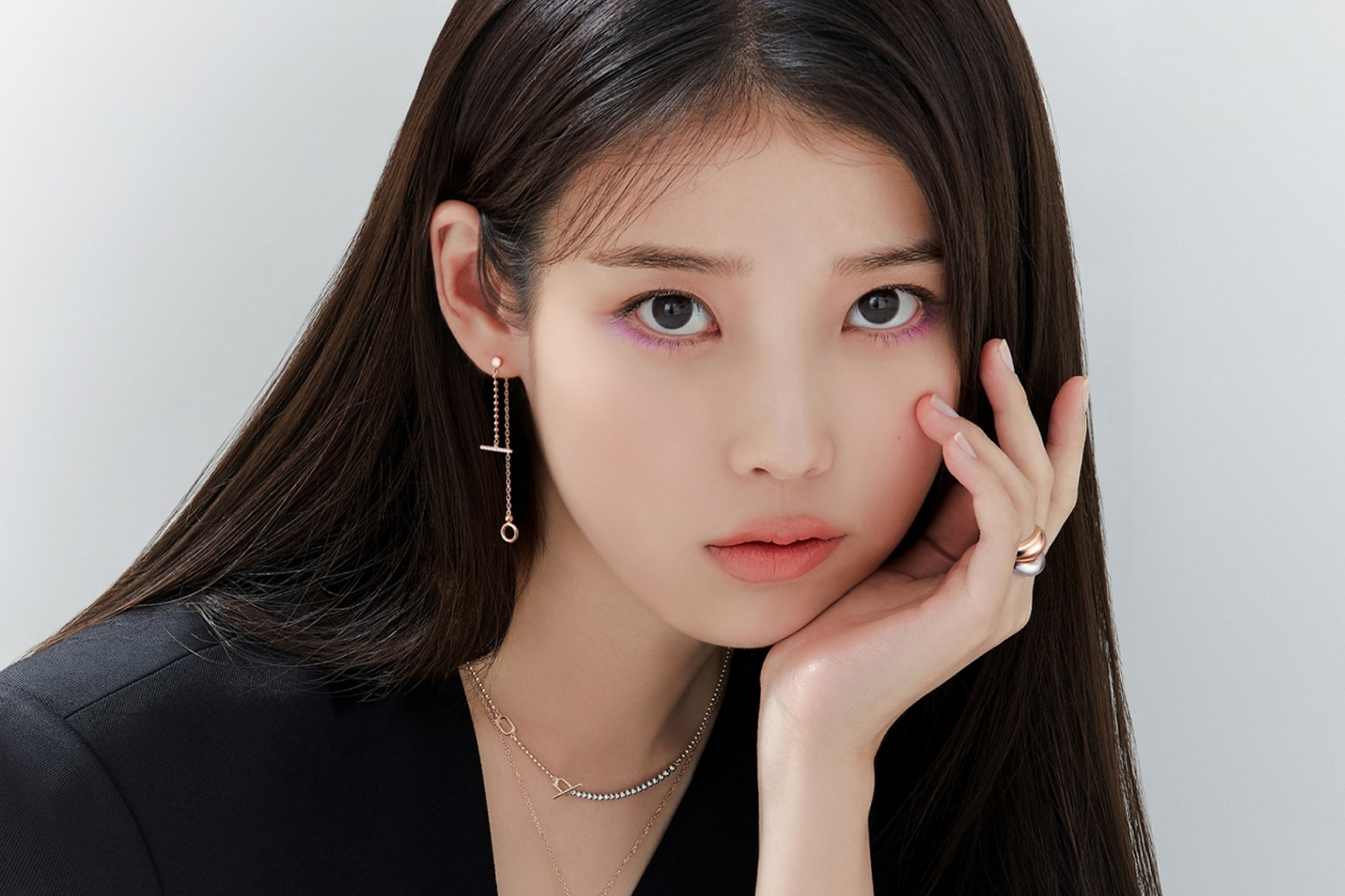IU 穿著黑色上衣，露出左側耳墜與項鍊，背景為淺灰色。