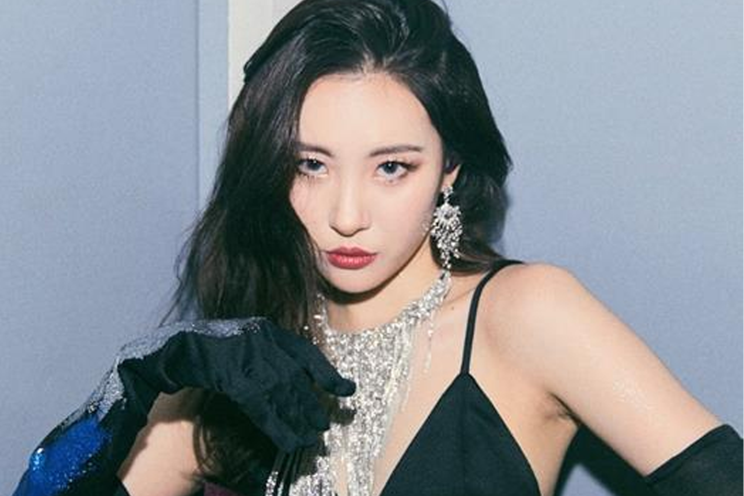 宣美身穿黑色禮服，搭配閃亮耳環和項鏈，背景為藍色。