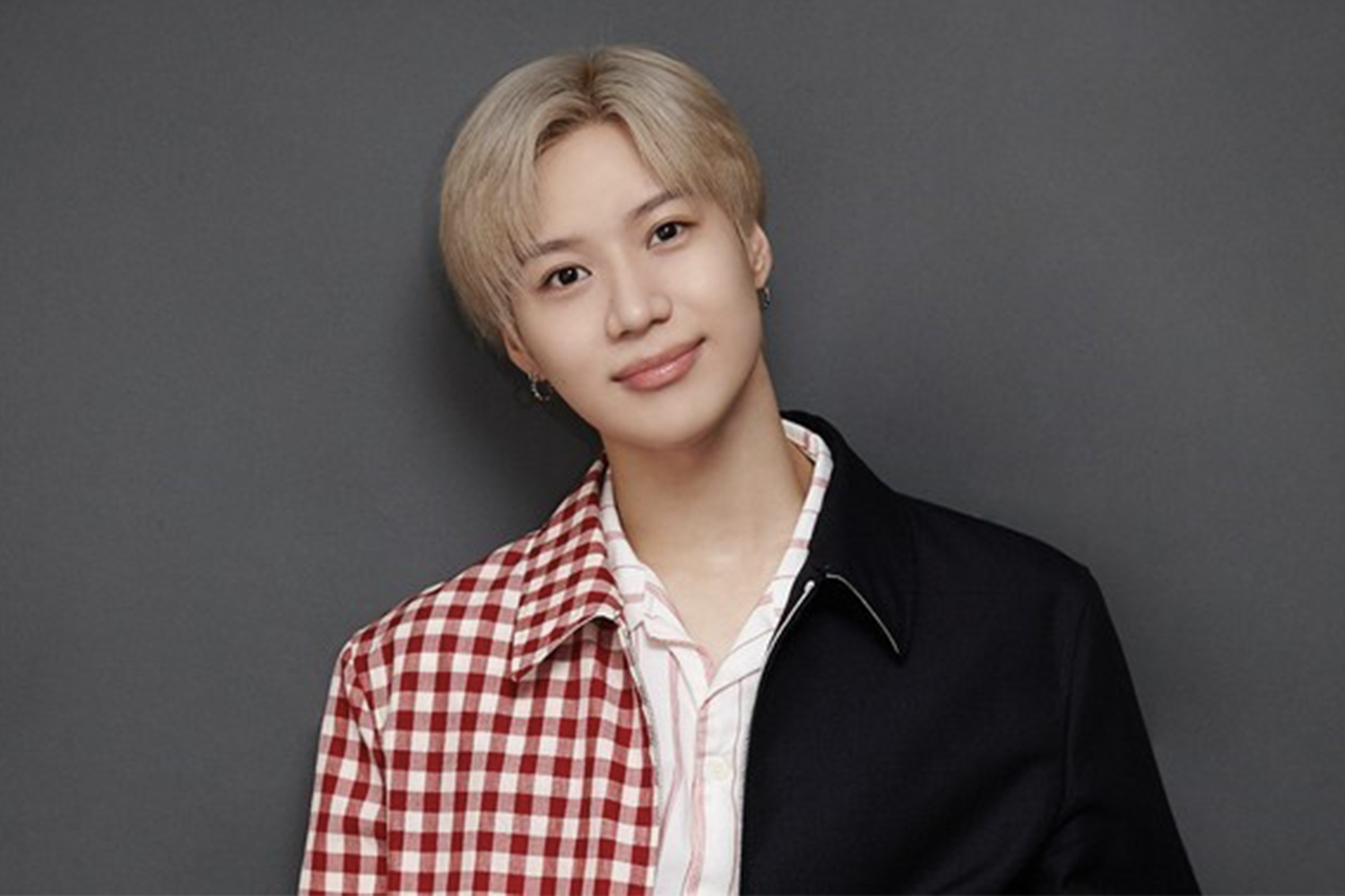 泰民穿著紅白格子外套，站在深色背景前。