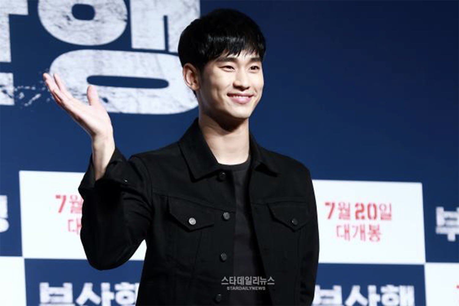 金秀賢身著黑色外套，出席電影首映活動，背景是藍色海報。
