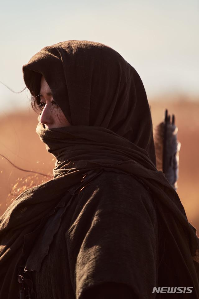 Netflixオリジナルシリーズ『キングダム : アシン伝』のスチールショット。砂漠の中でフードを被った人物が空の遠方を見つめているシーン。